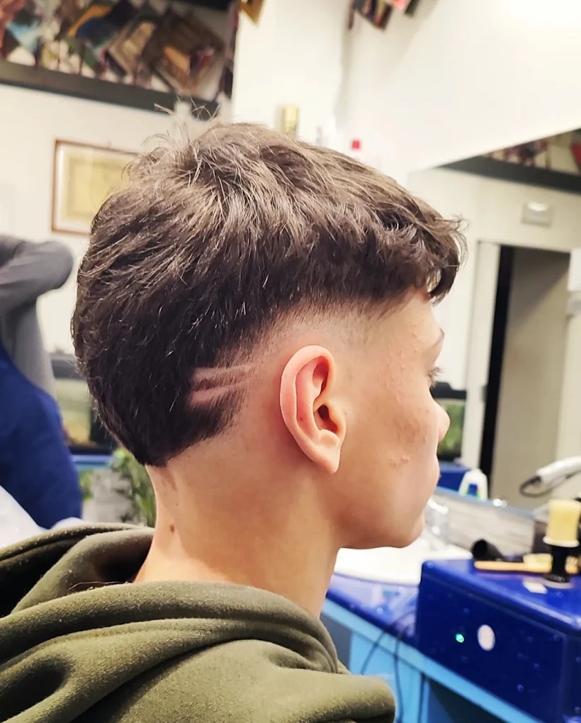 Taglio uomo con sfumatura laterale e riga incisa, capelli mossi sulla parte superiore